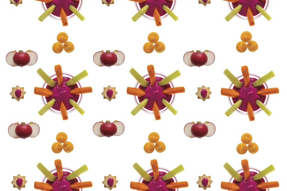 A kaleidoscope inspired pattern of a bowl with beet dip with carrots and celery sticks and slices of radish and veggies.