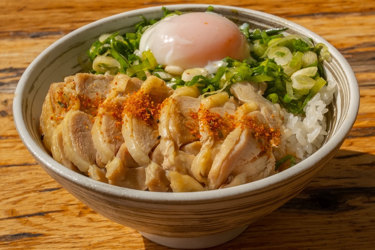 A bowl with rice, cooked slices of meat, a green onion mixture and a poached egg.