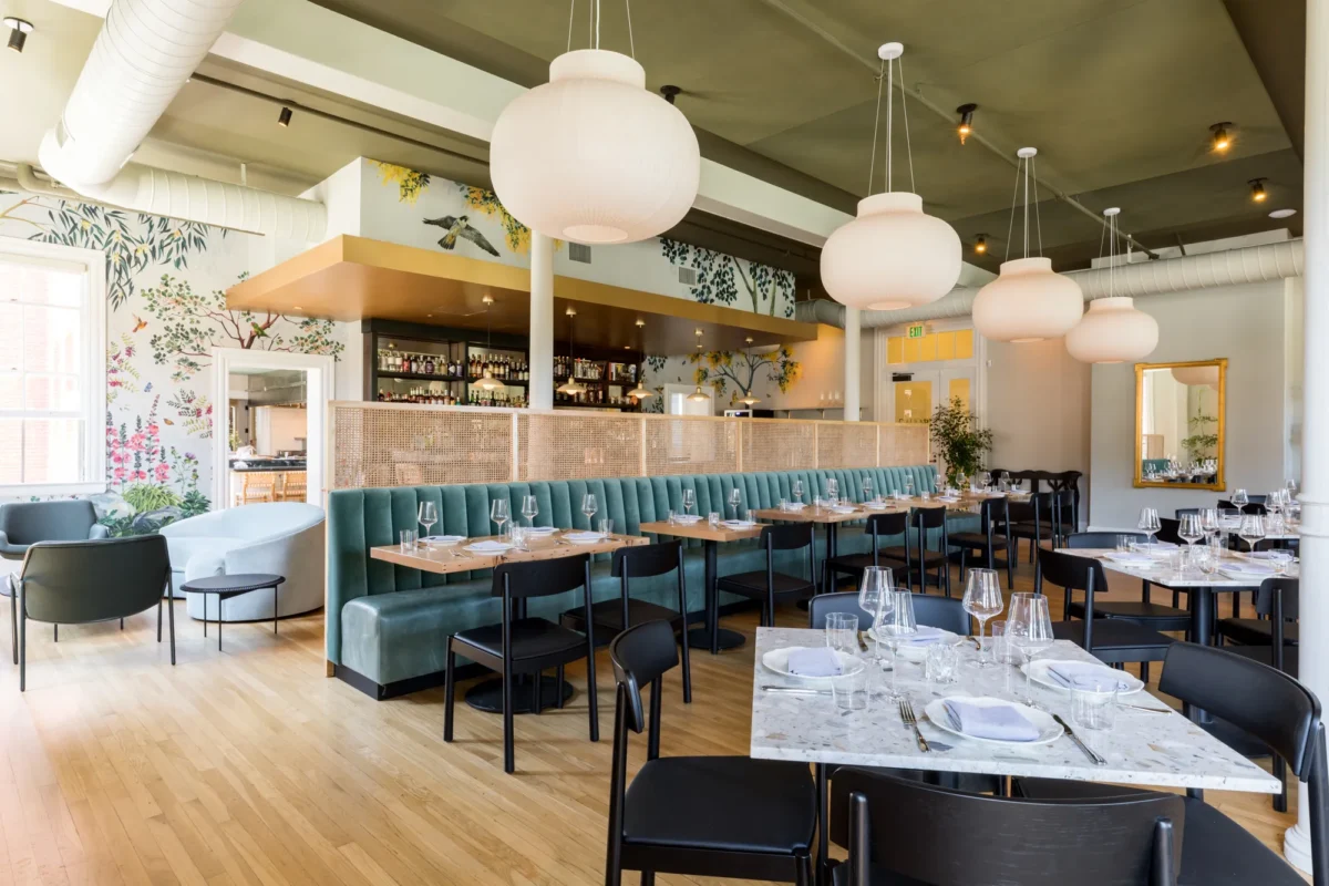 The interior of a restaurant with teal booths, tables set, handing circular lights and wood floors.