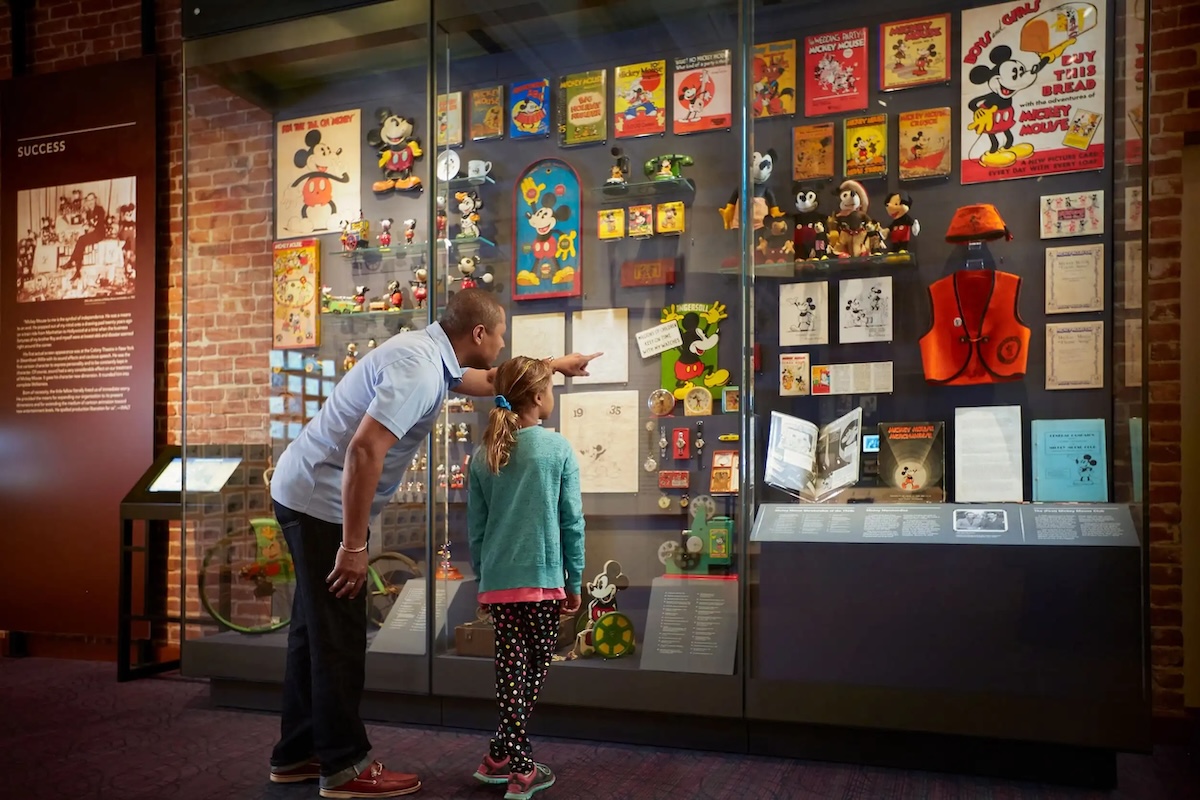 A father and daughter look at a museum display pointing at it.