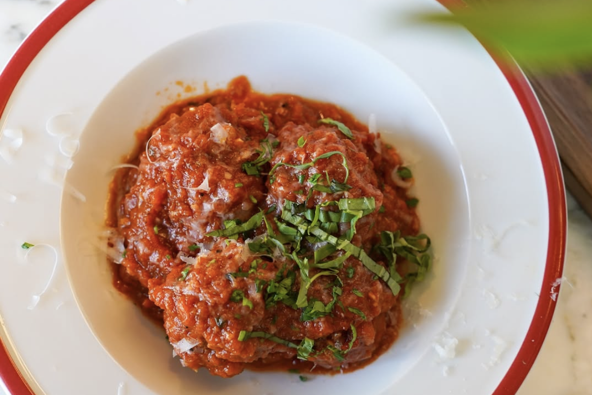 A white bowl with meat and red sauce pasta topped with sliced herbs.