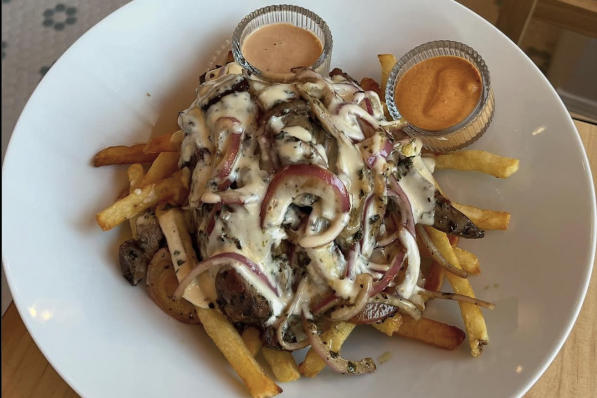 A plate with fried topped with a creamy sauce and some onions, with two mini bowls of sauce on the side.