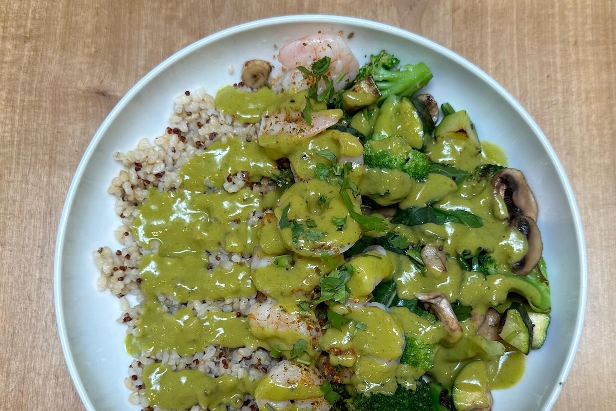 A plate with brown rice and quinoa, shrimp, mushrooms, broccoli, a green sauce and some cilantro.