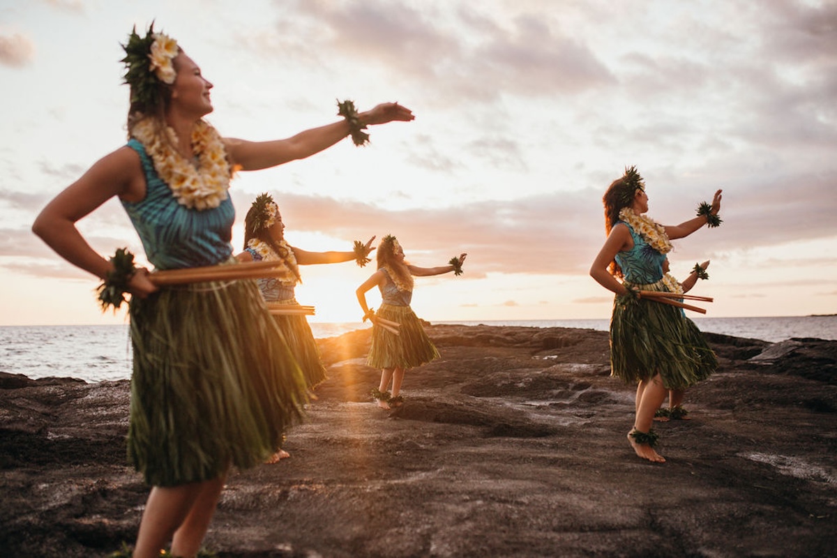 Four hula dancers performing on a rocky bluff next to the ocean.