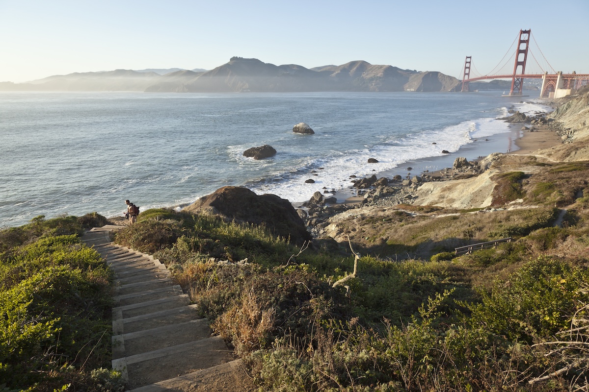 A view of the bay and the Golden Gate Bridge in the background and a wooden staircase leading down to the beach.