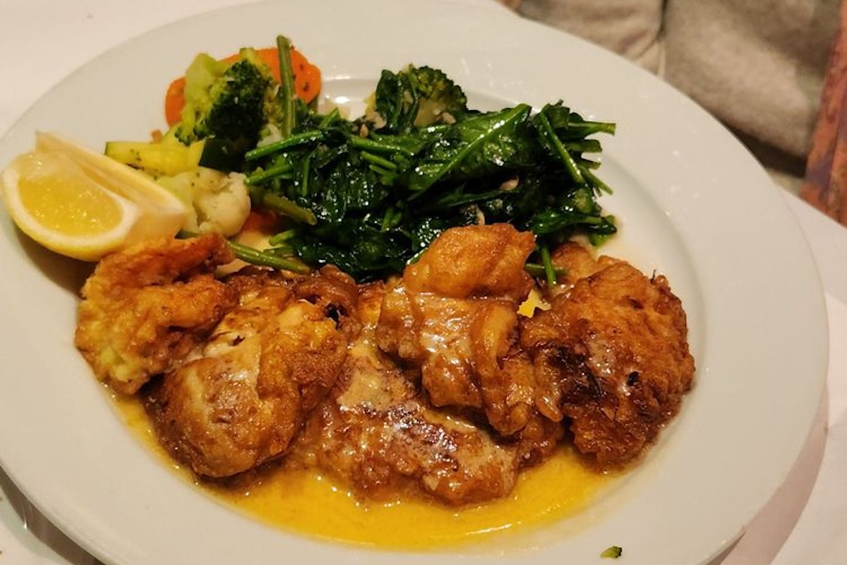 A plate of chicken in a yellow sauce with a side of veggies, greens and lemon slices.