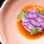 A plate with purple circular food plated with sauce and garnish.