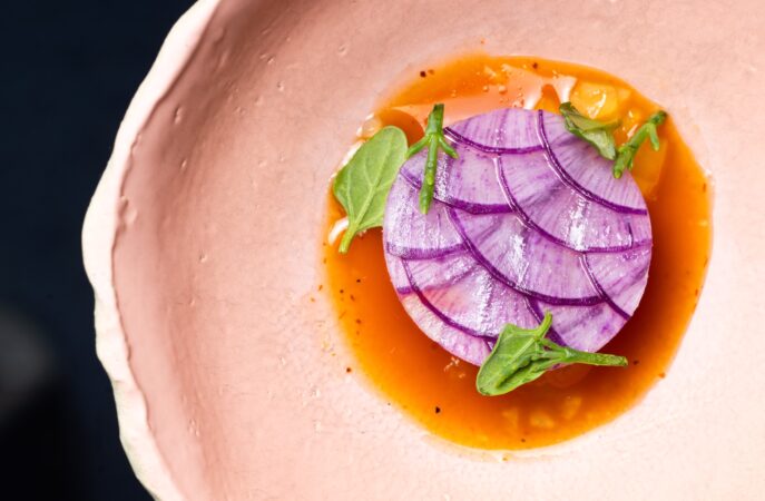 A plate with purple circular food plated with sauce and garnish.