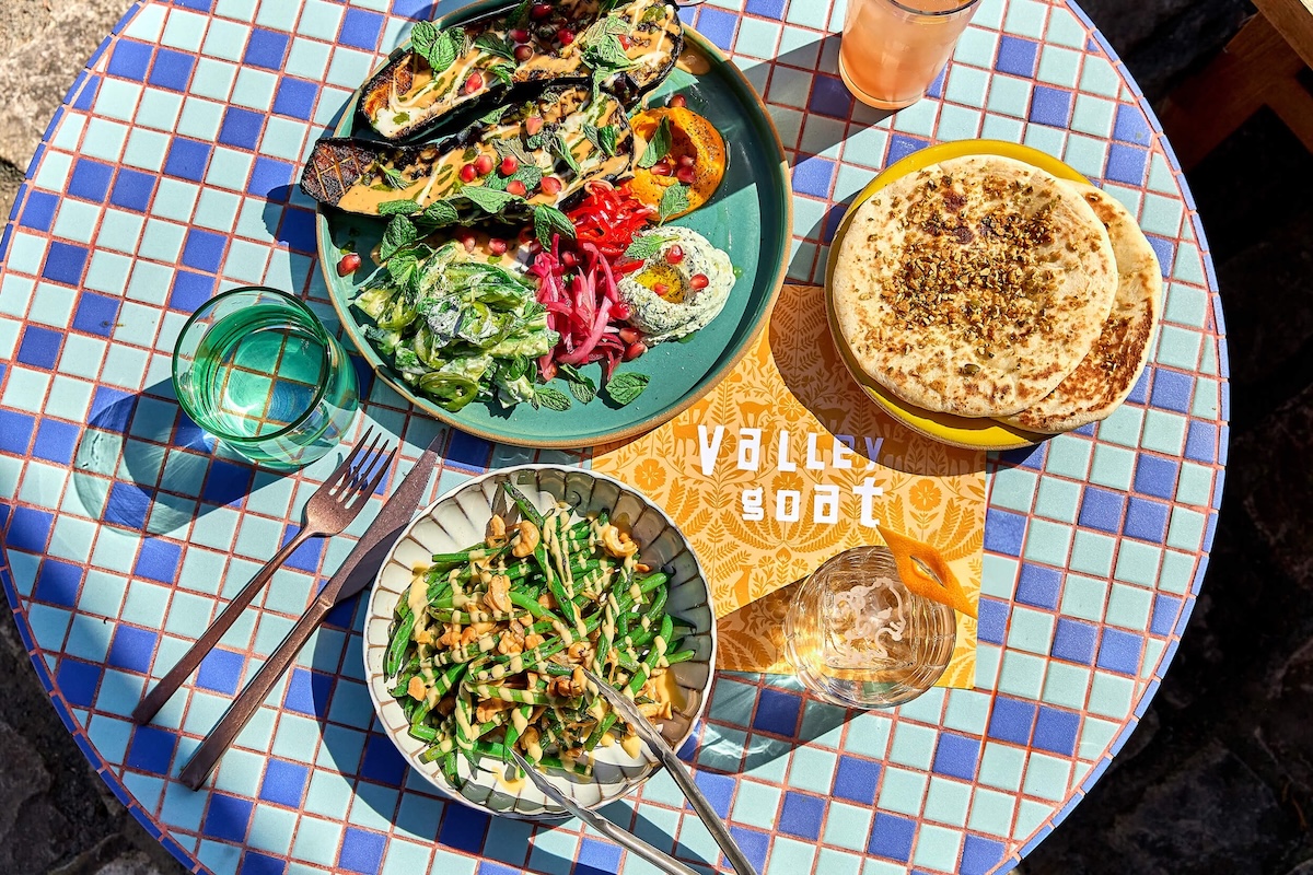 On top of a blue tiled round table sits plates of colorful food and drinks.