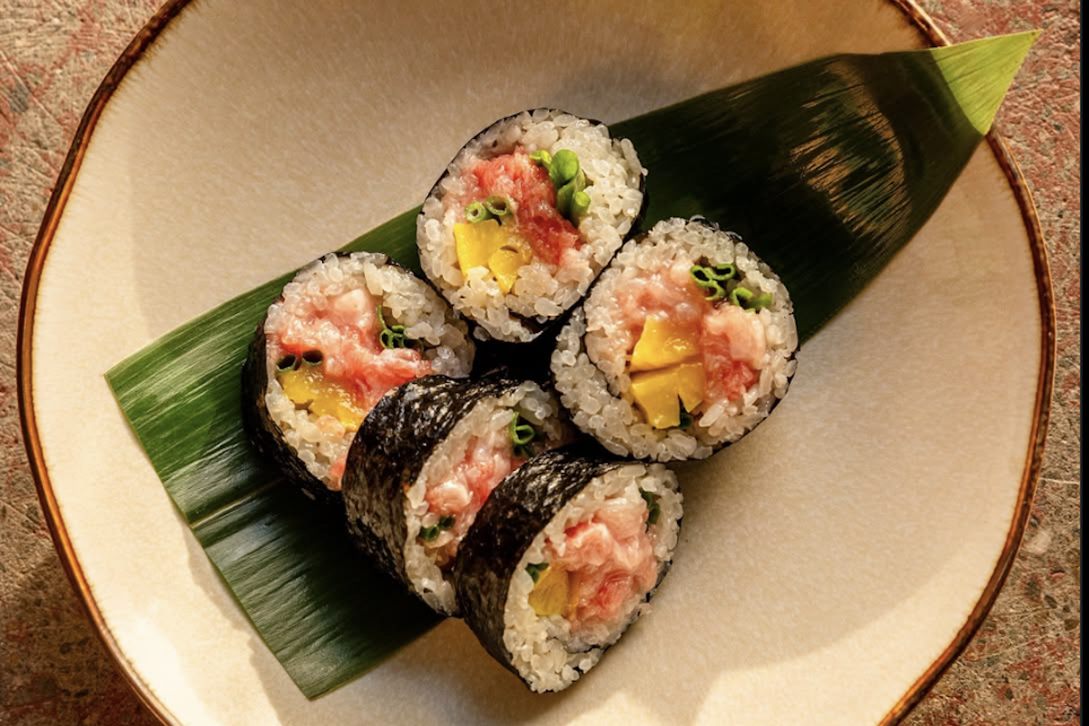 Five cuts of sushi with some yellow, pink and green interior sit on a leaf.