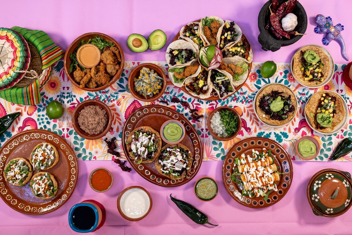 An aerial shot of a pink table with lots of plates of vegan Mexican food and sauces, salsas and guacamoles.
