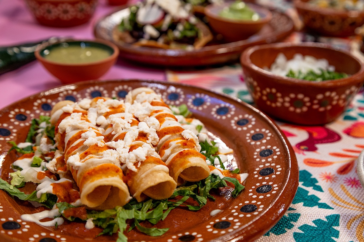 A close up shot of three rolled tortillas on a bed of lettuce and topped with red sauce and white sauce drizzles.