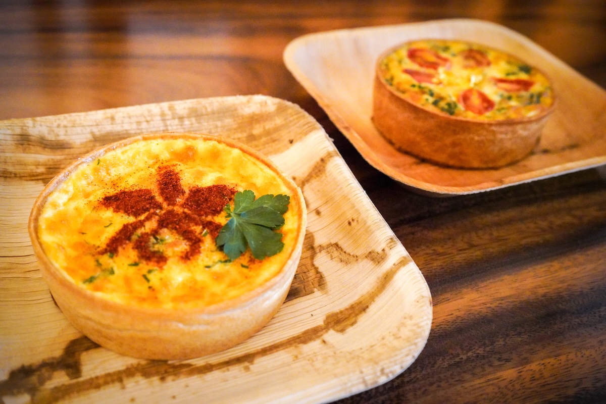 A couple of bamboo plates with quiches topped with a seasoning flower and herbs for garnish.