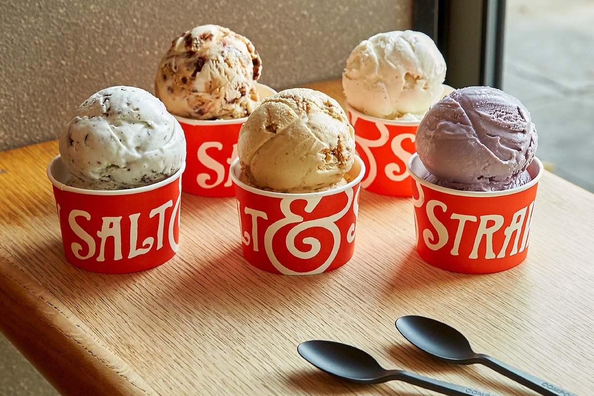 Five red containers with ice cream scoops sit on a wooden counter.