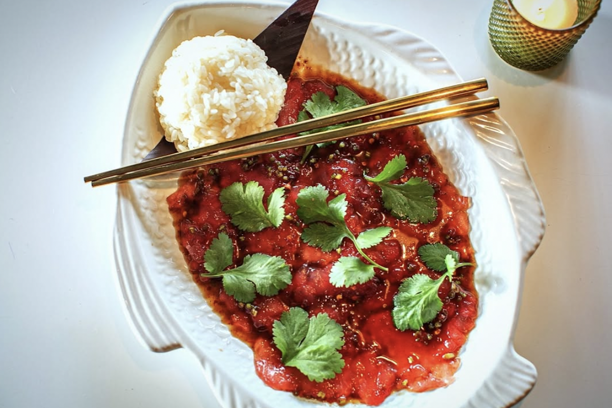 A fish-shaped plate with a red saucy dish, rice on the side and chopsticks resting on top.