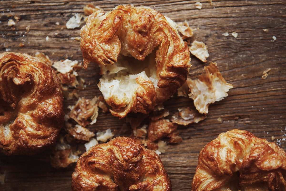 Flaky, golden-brown Kouign-amann pastries on a rustic wooden surface.