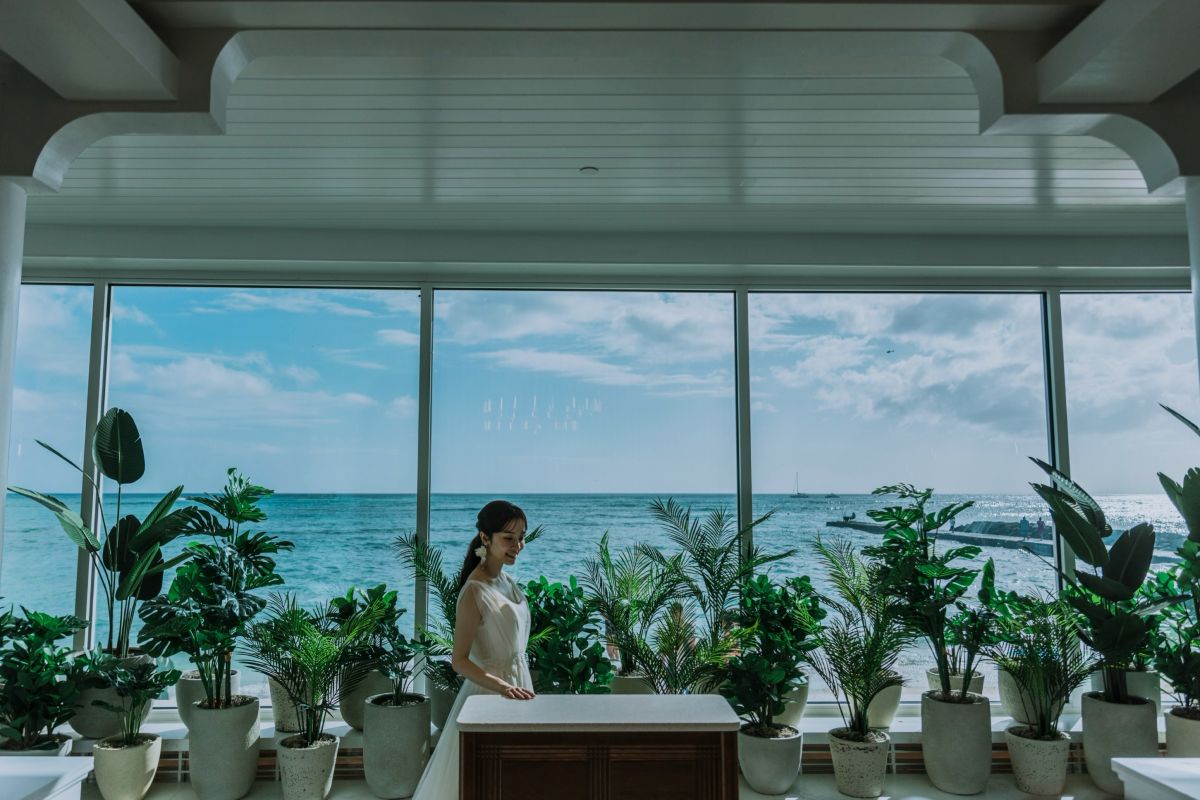 Bride stands at the altar of Kahawai Chapel with ocean views framed by large windows.