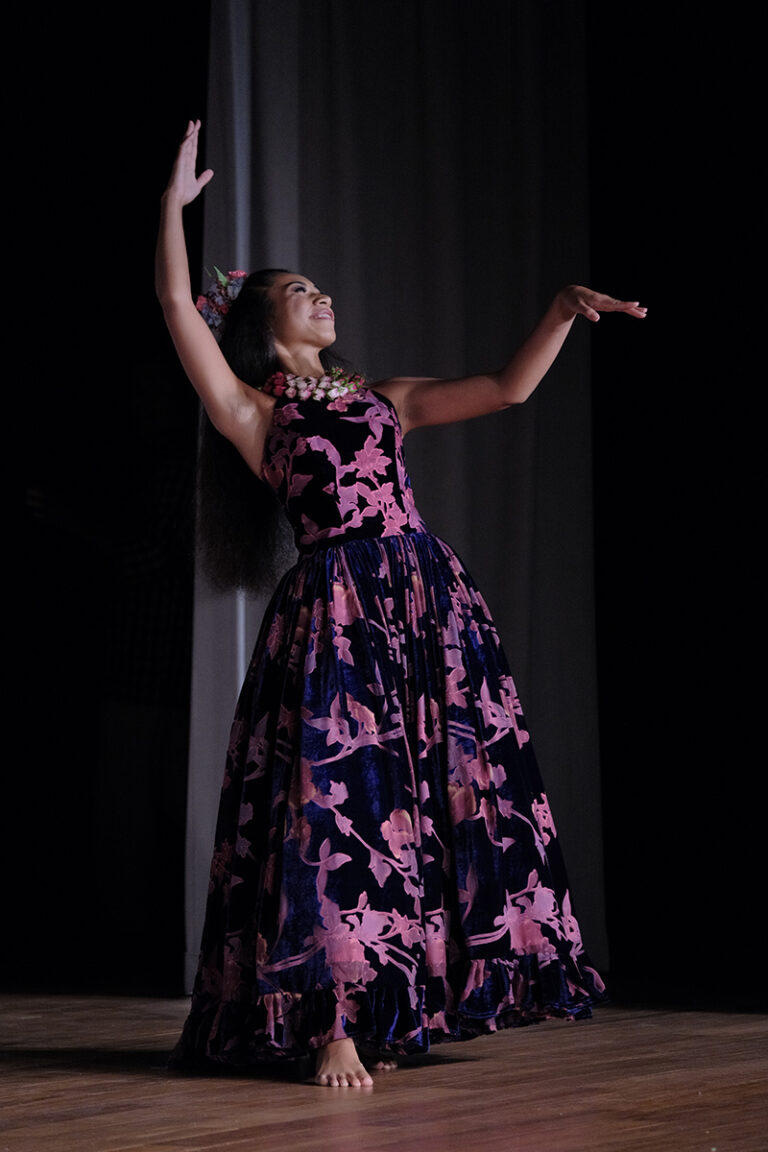 A woman dressed in purple dances expressively, highlighting her skill and passion through movement.