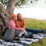A man and woman relax on a blanket beneath a tree, enjoying a peaceful moment together in nature.
