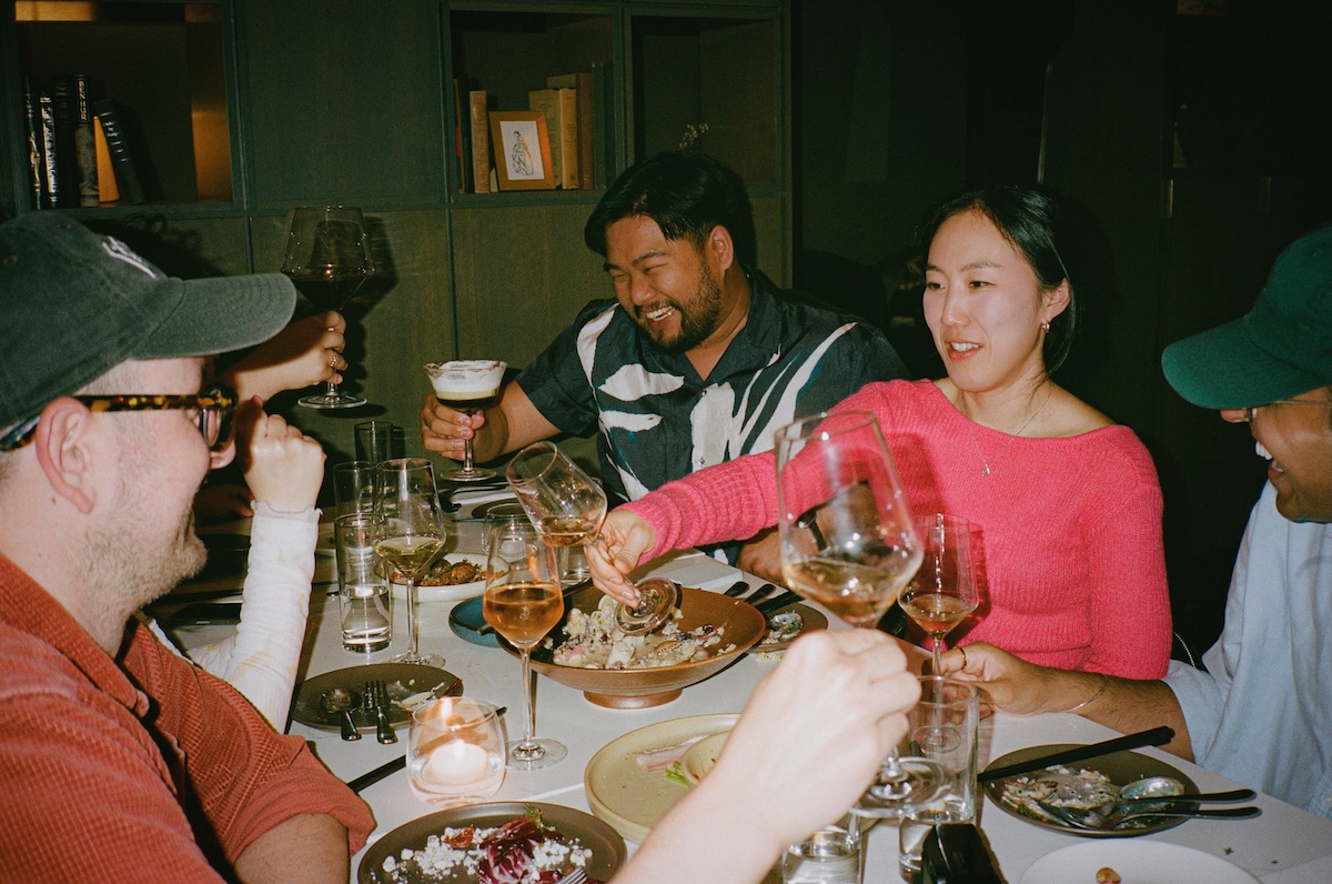 People sit around a table with lots of plates of food and drinks.