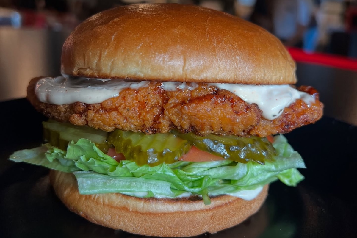 A fried chicken sandwich with pickles, lettuce, tomato and white sauce.