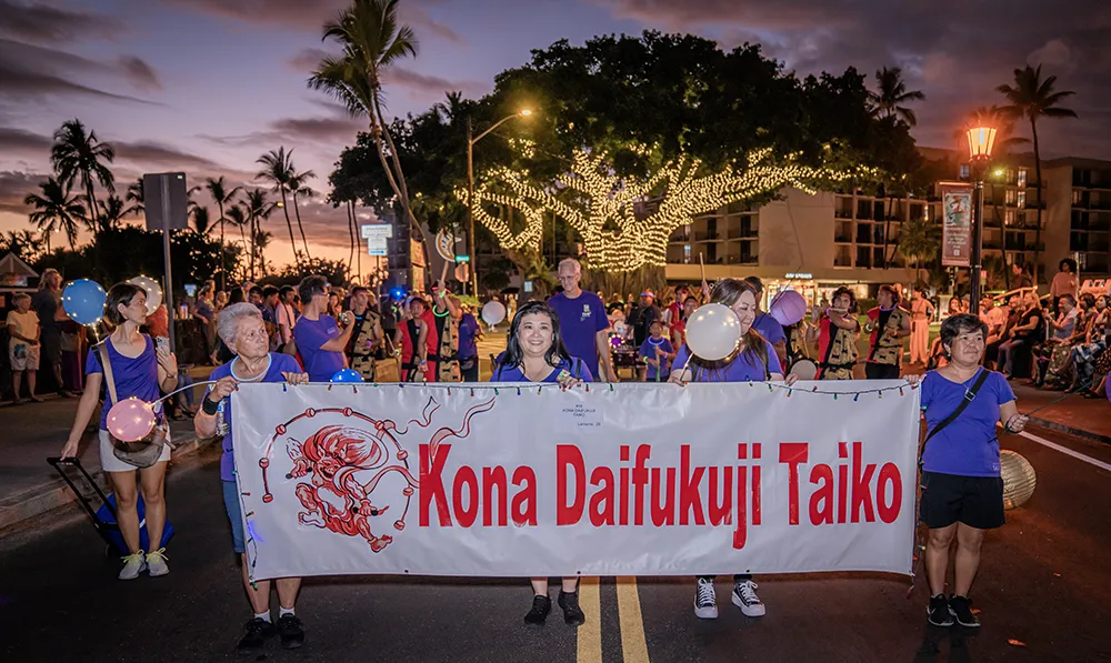 A diverse group of people stands together, holding a banner in a public space.