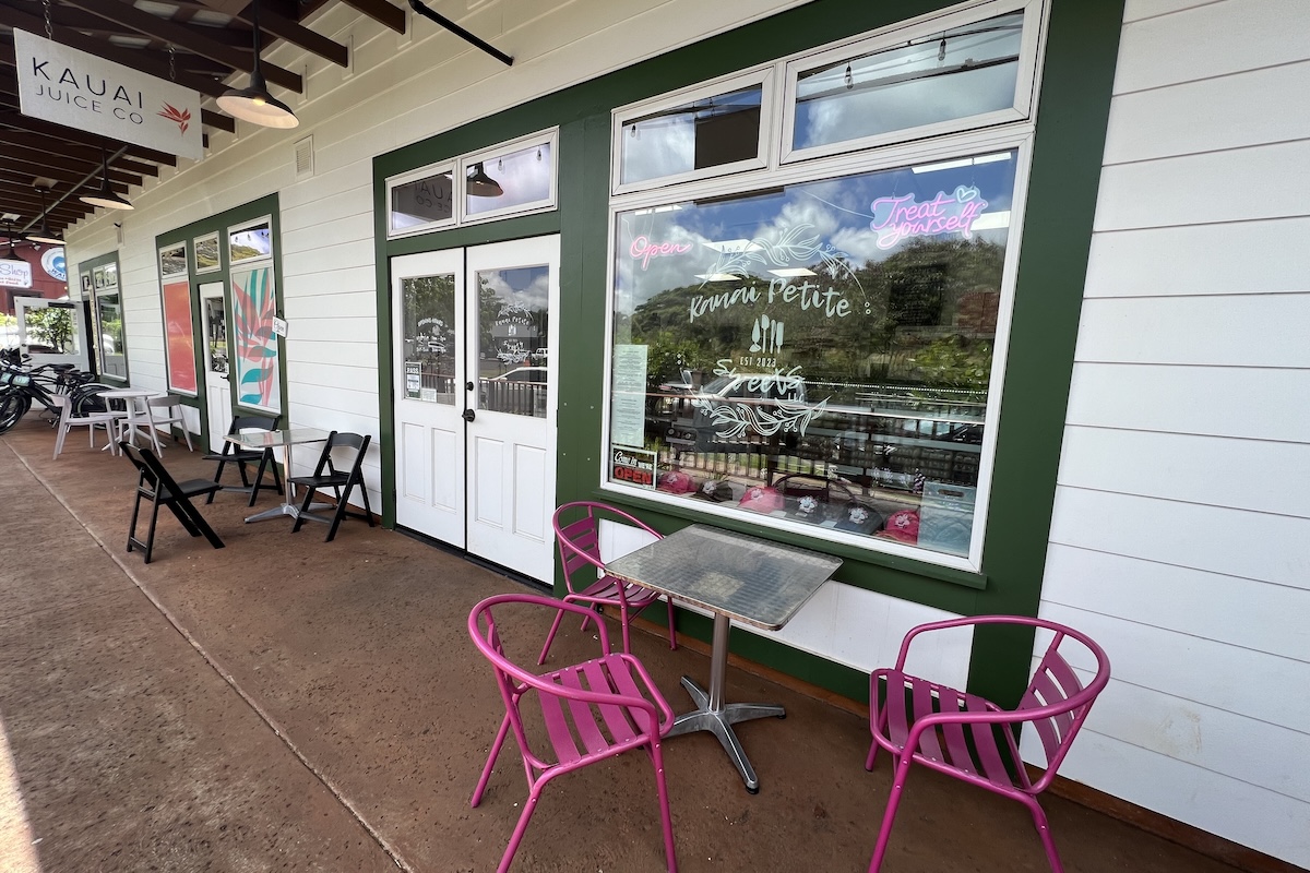 The outside of a restaurant with pink chairs and outdoor dining.