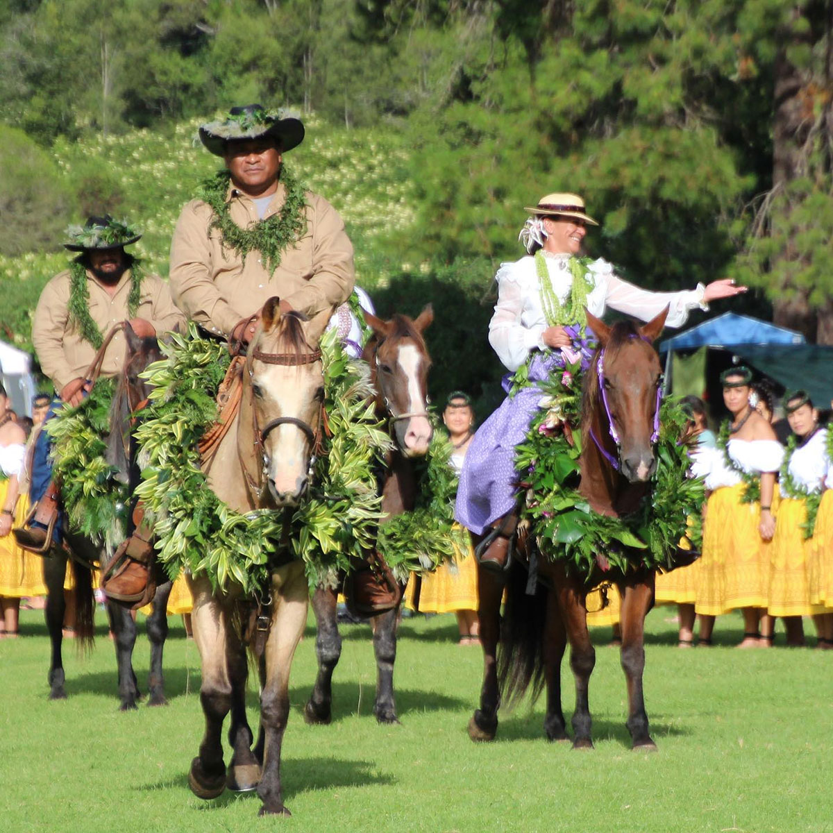 A group of people riding horses across a green field under a clear blue sky.