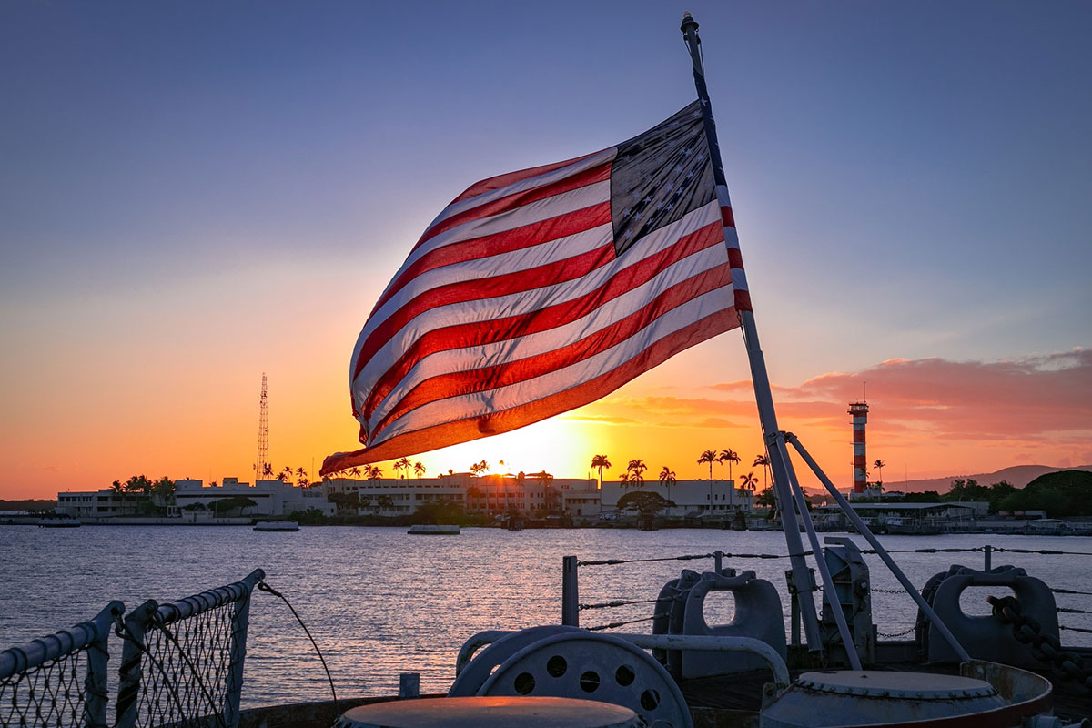 The American flag flutters on a boat as the sun sets, casting a golden glow over the scene.