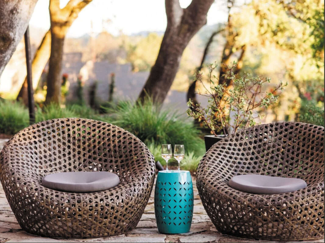 A pair of wicker chairs flanking a table with two wine glasses, creating an inviting space for relaxation.