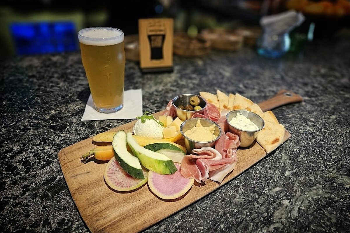 A wooden charcuteries board with various cheeses, dipping sauces, olives, meats and pita.