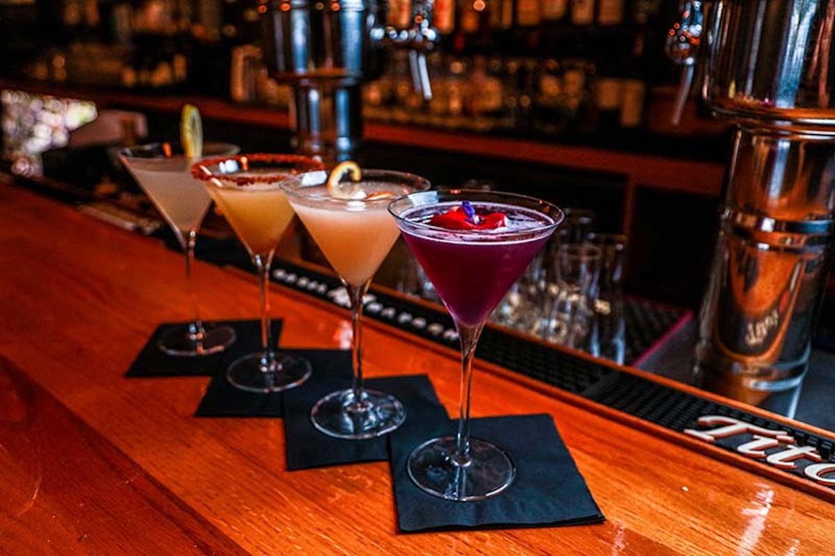 An assortment of cocktails lined up on a bar, featuring vibrant colors and decorative garnishes.