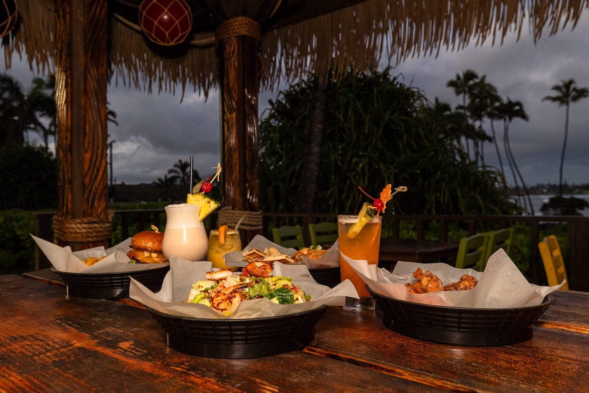 Plates of food and a pina colada on an outdoor dining table.