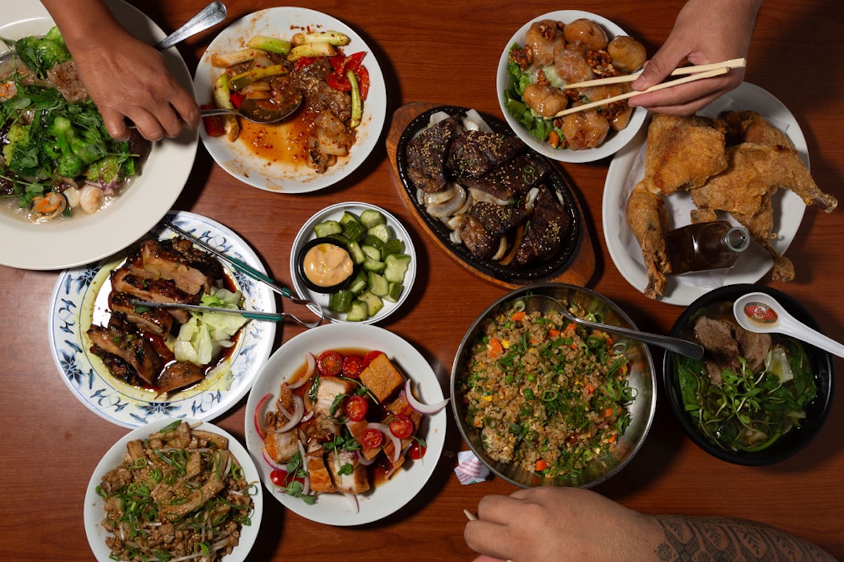 An aerial shot of lots of plates of food and people reaching with chopsticks.