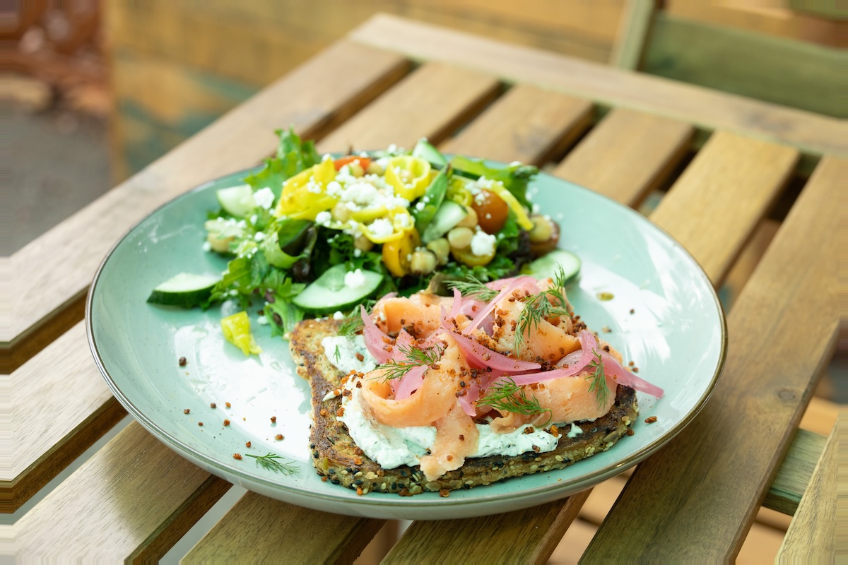A blue plate with toast topped with lox, cream cheese and dill, and a side of salad.
