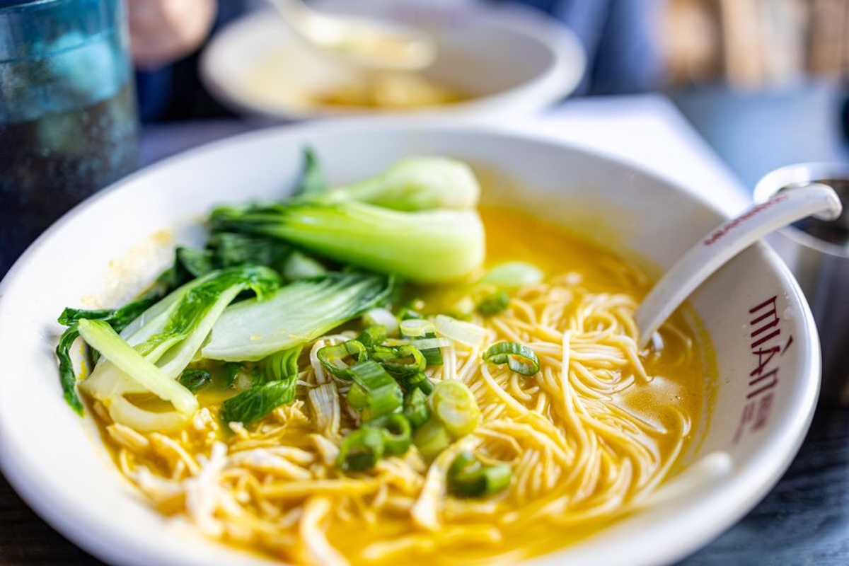 A bowl of noodles topped with bok choy and sliced green onions.