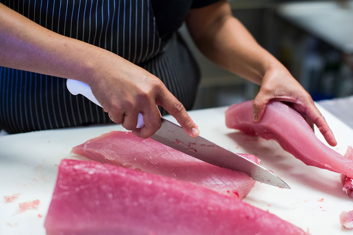 A person slicing fish on a cutting board with a sharp knife