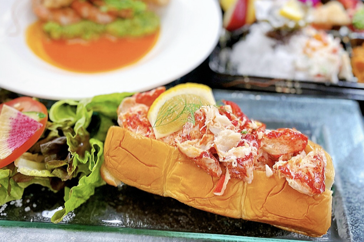 A lobster roll topped with a lemon slice and lettuce on the side.