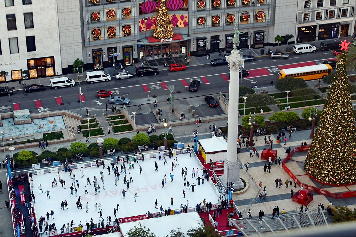 A vibrant city square showcasing an ice skating rink filled with skaters, framed by holiday lights and buildings.