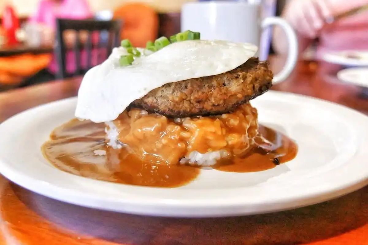 A patty sits on top of a bed of rice covered in sauce and topped with a fried egg.