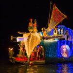 A boat illuminated by lights floats gently on the water at night.