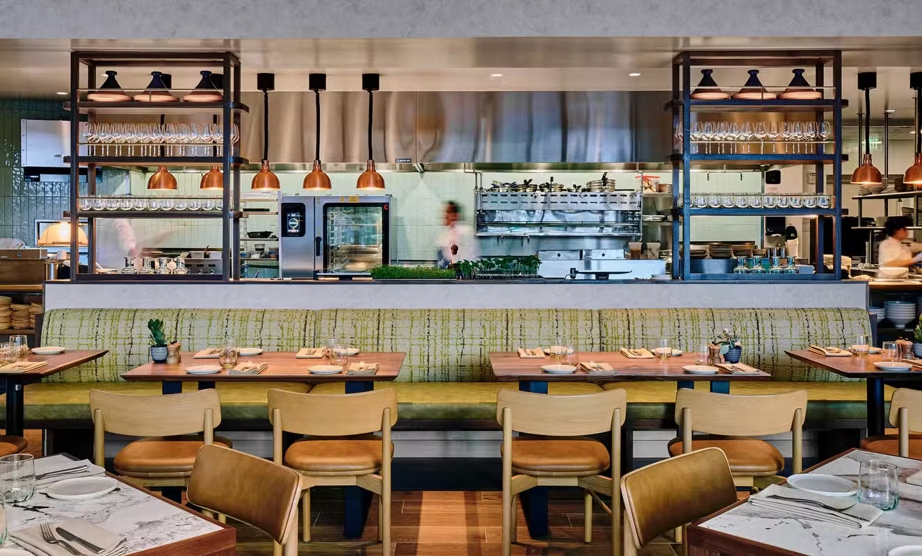 A restaurant with a view into the kitchen and tables set for dinner.