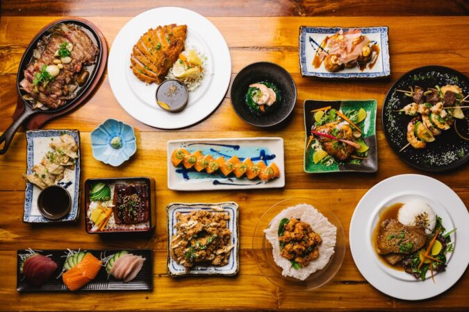 An aerial shot of various plates of food, including sushi, cuts of different meats, potstickers and more.