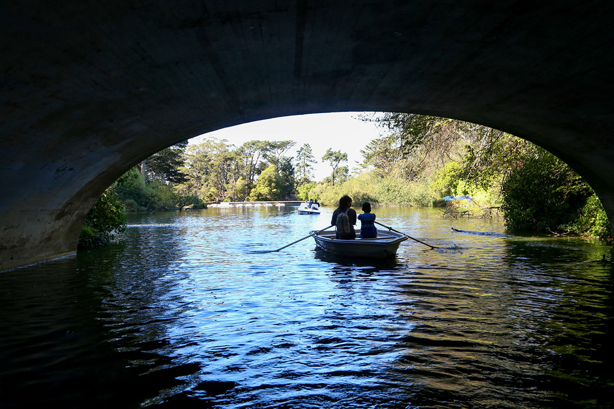 Two people paddle together in a small boat on a calm river, framed by trees and gentle ripples.