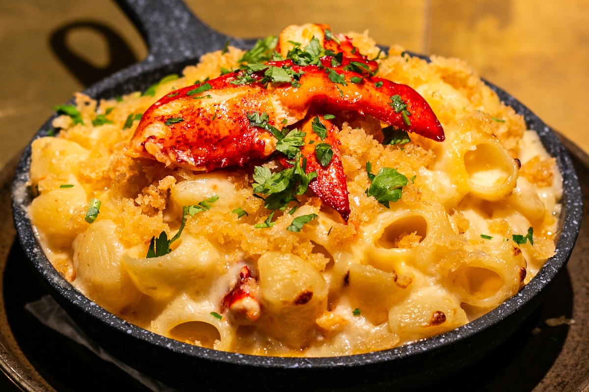 A bowl of lobster mac and cheese topped with chopped herbs and a lobster claw for garnish.