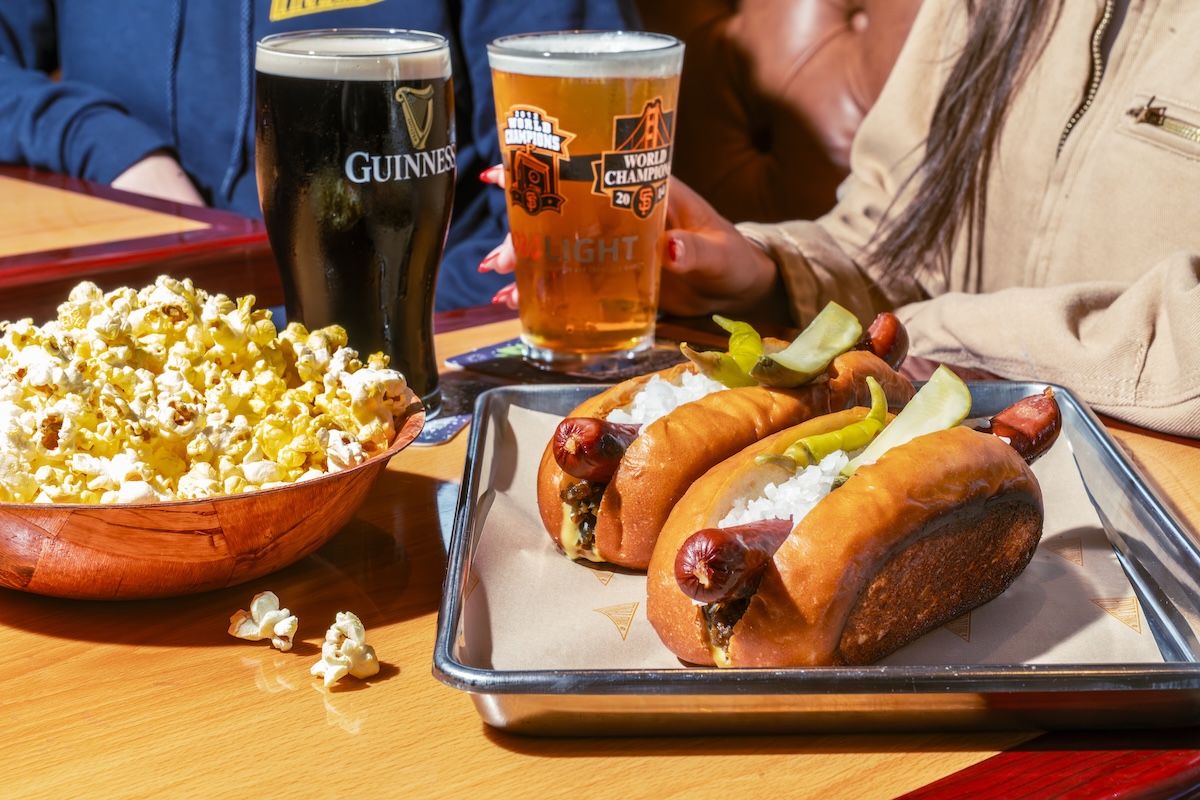 A tray of two hot dogs, a bowl of popcorn and two beers.