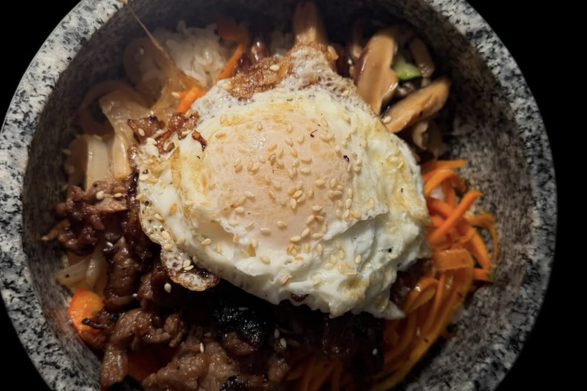 A granite bowl with a stir fry of sorts, topped with a scoop of sauce.