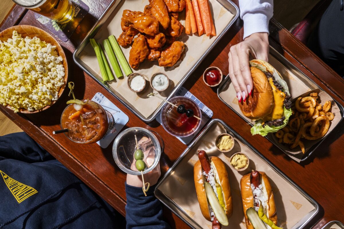 An aerial shot of trays with buffalo wings, hot dogs, popcorn and classic cocktails.