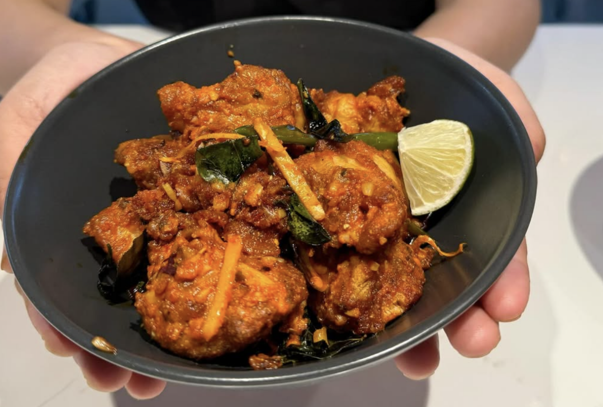 Someone holds a black bowl with fried meat coated in a red sauce.
