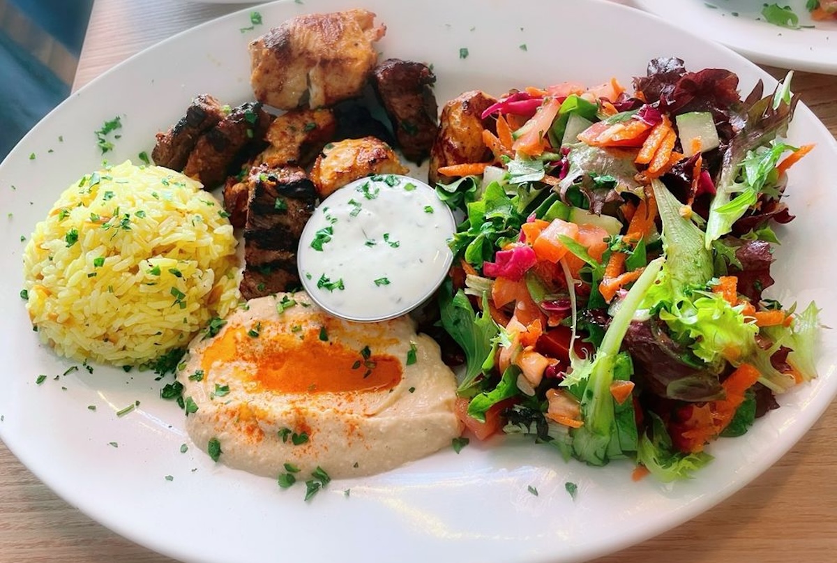 A plate with rice, hummus, meat and a side salad.